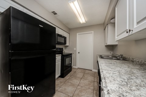 A kitchen with a black fridge and a sink with a marble counter top.