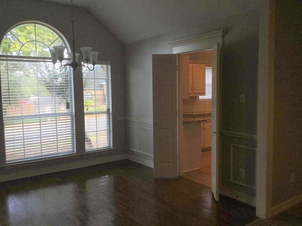 an empty living room with a large window and a door to a kitchen