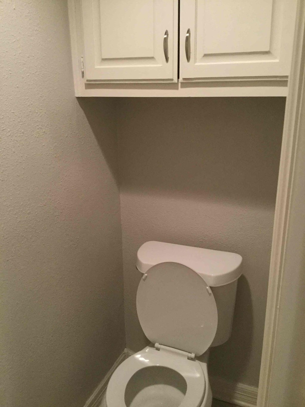a small bathroom with a toilet and cabinets above it