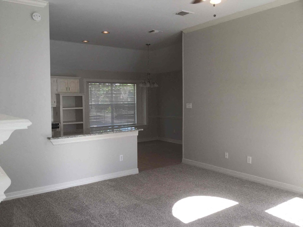 an empty living room with a kitchen and a window