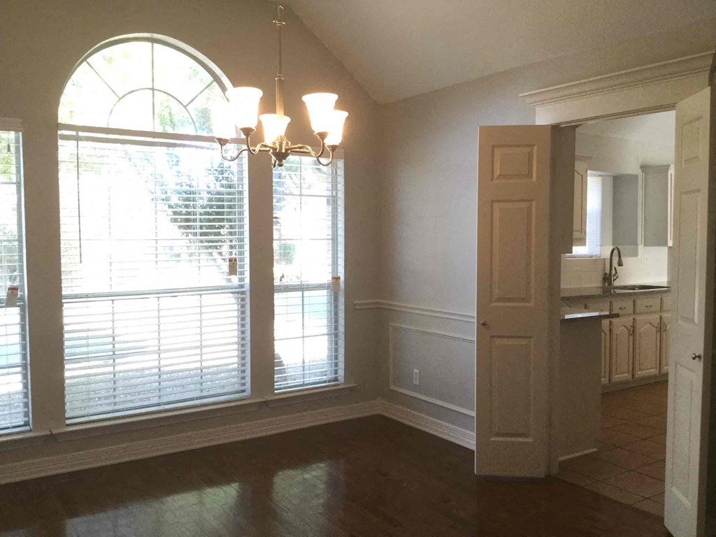 an empty dining room with large windows and a door to the kitchen