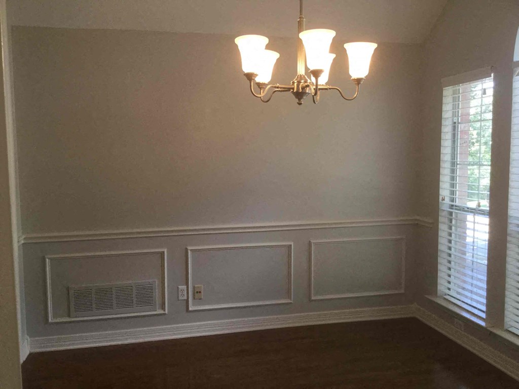 an empty dining room with wainscoting and a chandelier