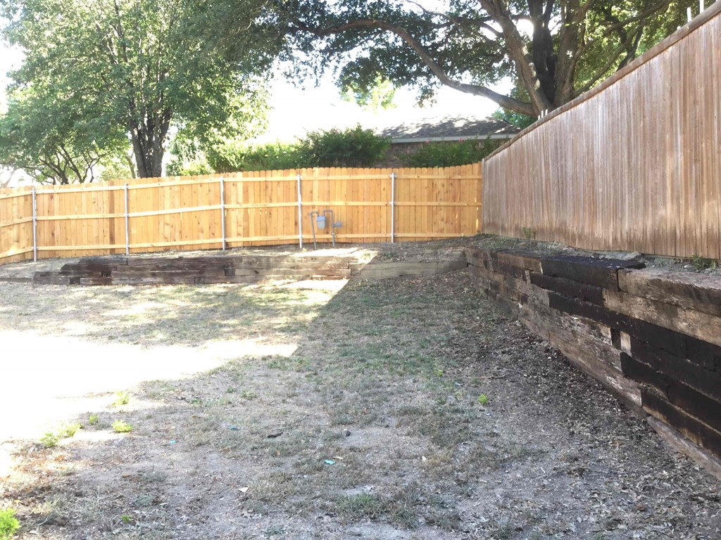 a backyard with a wooden fence and a retaining wall