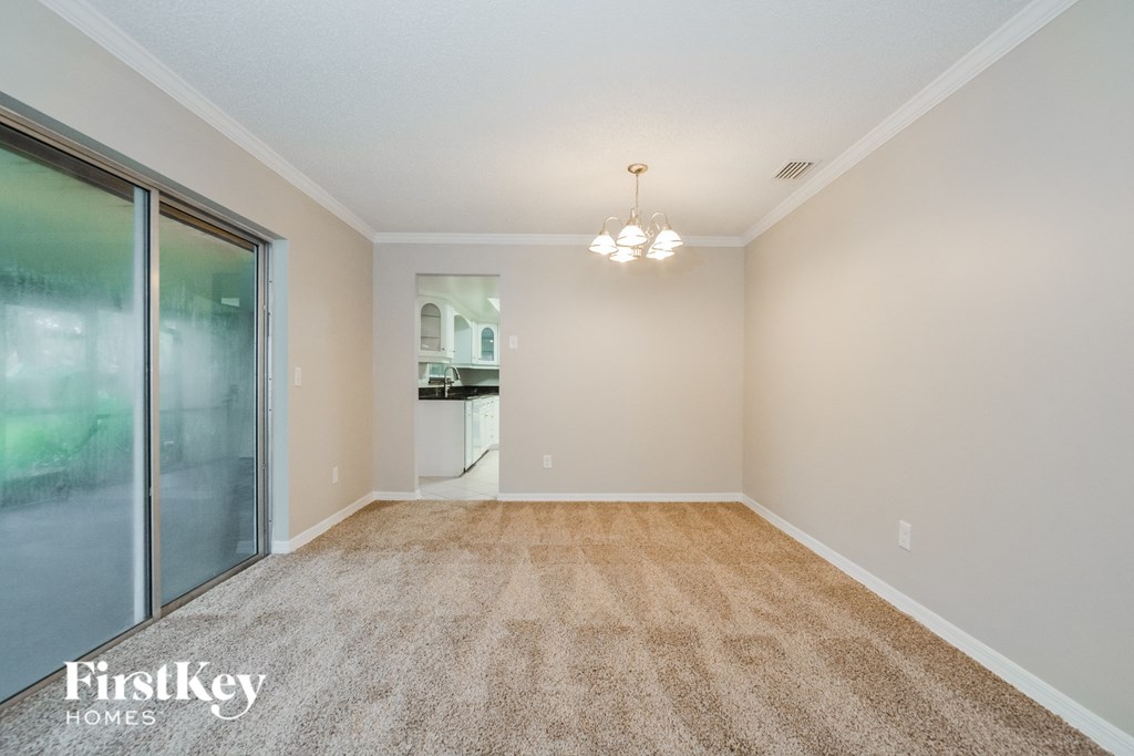 A carpeted room with a sliding glass door and a small kitchenette in the background.