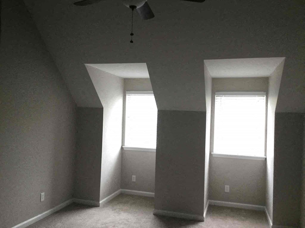 an empty room with two windows and a ceiling fan