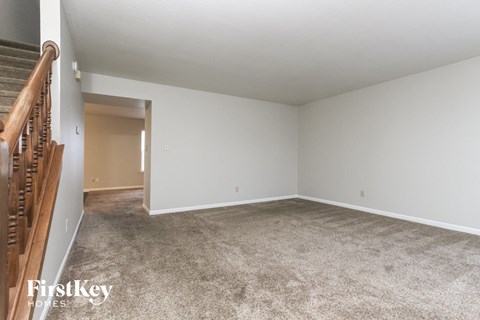 A spacious empty room with a carpeted floor and a staircase on the left side.