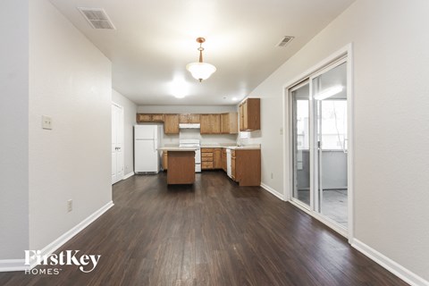 A room with wooden floors and a kitchen area with white appliances.