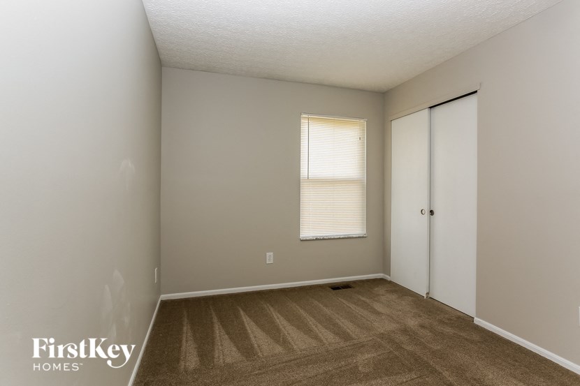 the living room of an apartment with carpet and a door to a closet