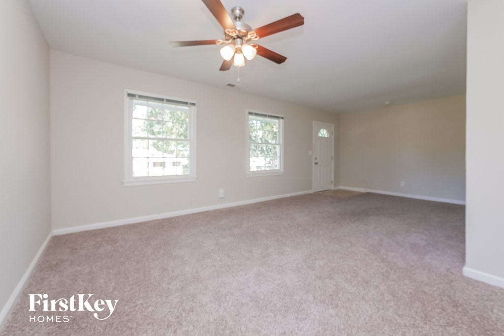 an empty living room with a ceiling fan and two windows
