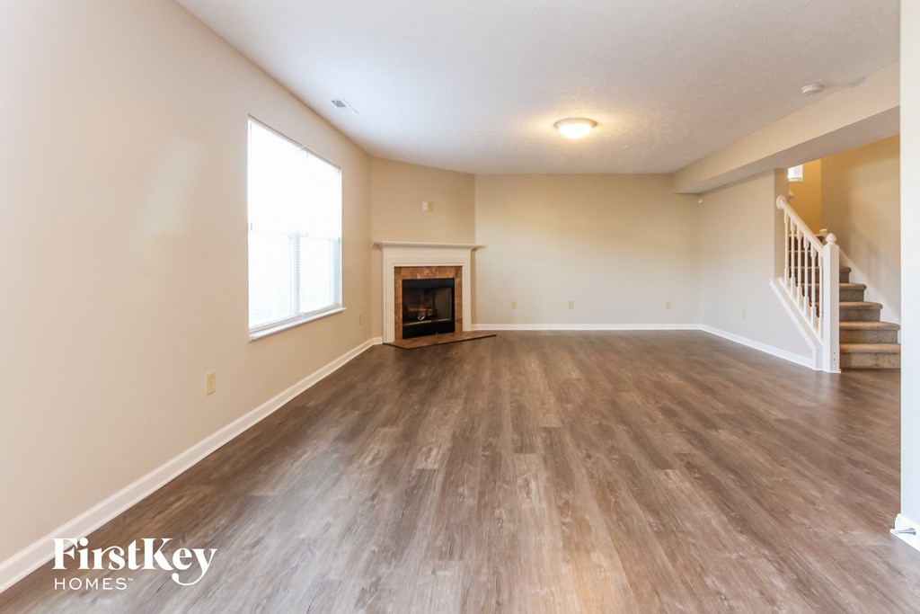 A spacious room with wooden flooring and a staircase on the right side.