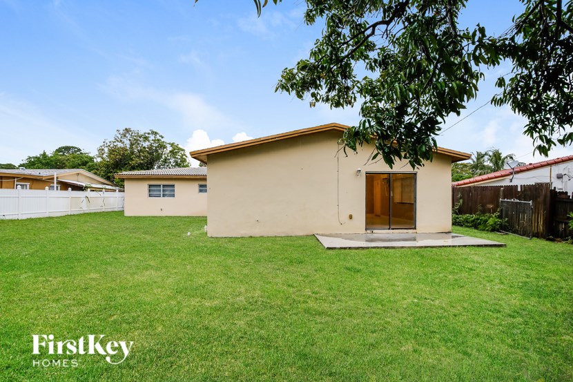A beige house with a brown door is surrounded by a grassy area.