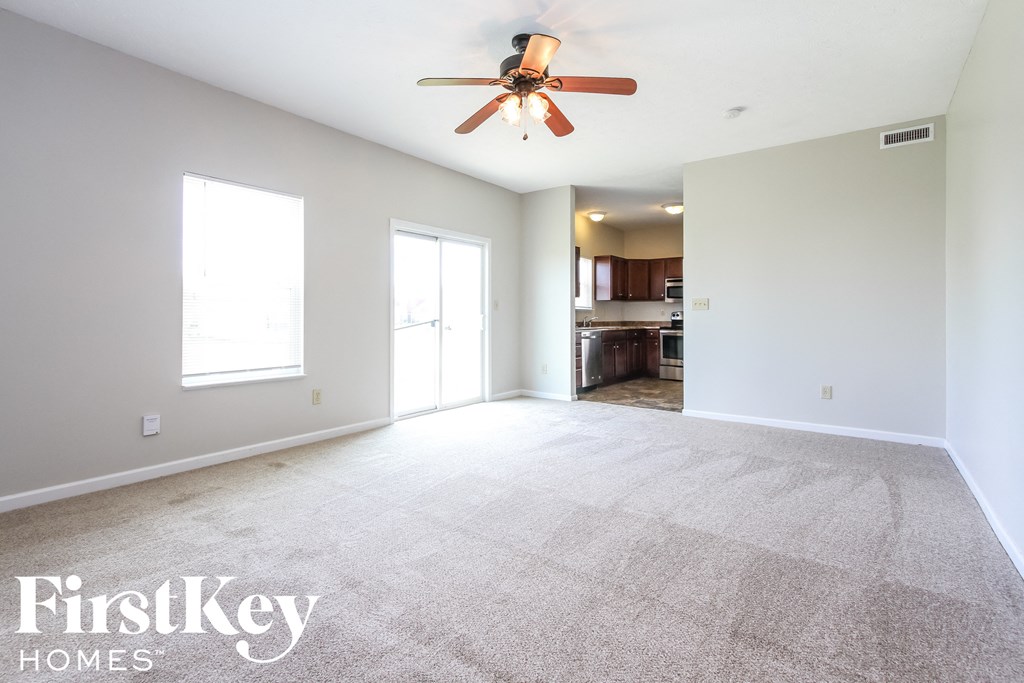 an empty living room with a ceiling fan and a kitchen