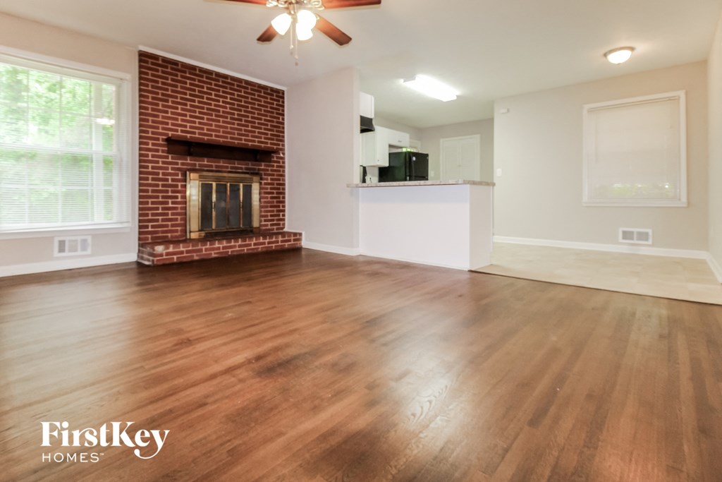 an empty living room with a brick fireplace and wooden floors