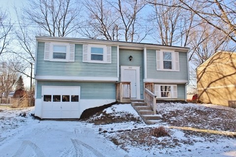A two-story house with a garage is surrounded by snow.
