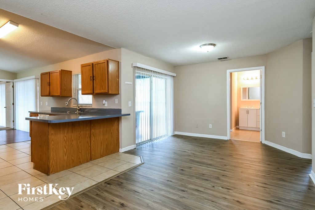 an empty kitchen and living room with wood flooring and a door to the bathroom