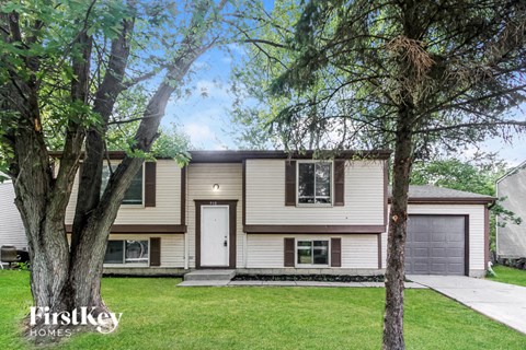 A house with a white door and a garage door is surrounded by trees.
