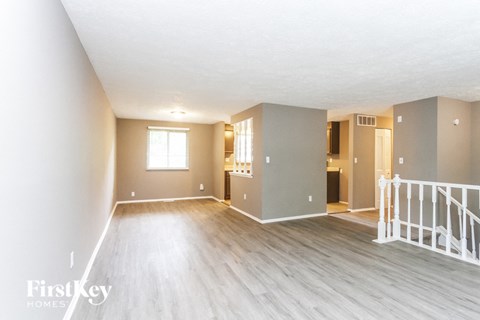 A spacious room with wooden floors and white walls, with a staircase leading to another room.