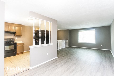 A spacious living room with wooden flooring and a window with blinds.