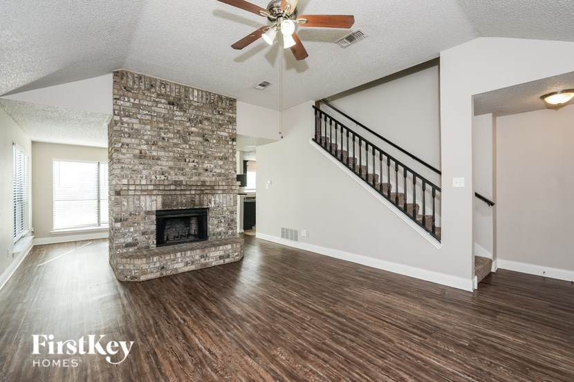 A spacious living room with a stone fireplace and a staircase.