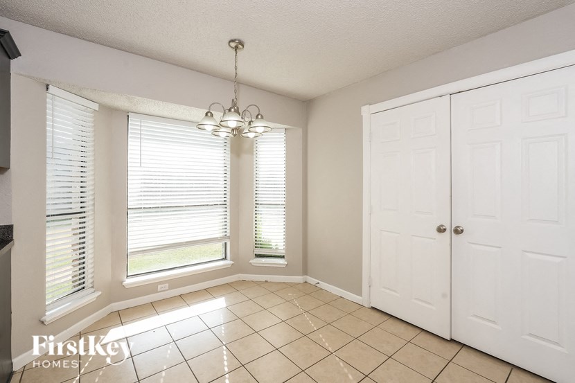 A room with a chandelier, a window with blinds, and a white door.