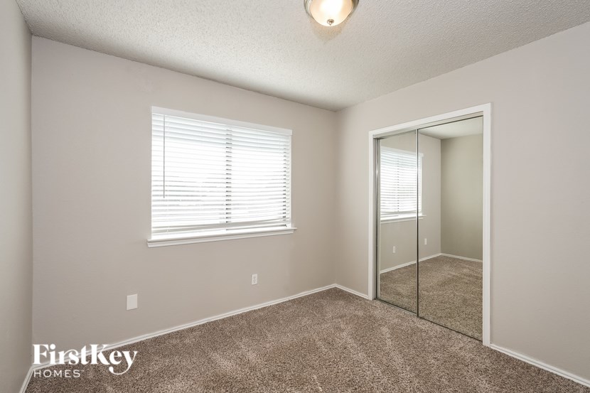 A room with a carpet floor, a window with blinds, a mirror, and a door.