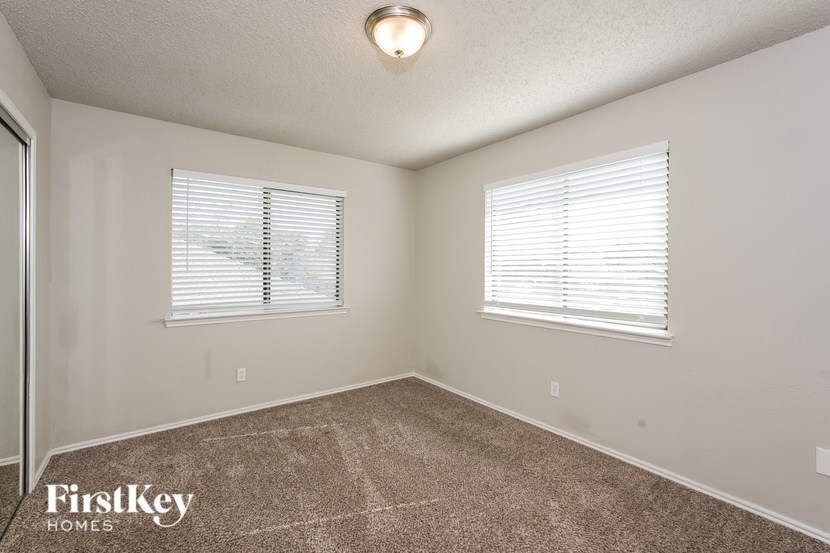 A room with a carpeted floor and two windows with blinds.