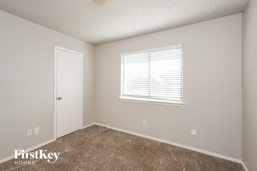 A room with a carpeted floor, a window with blinds, and a door.