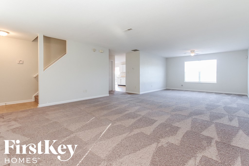A spacious room with a carpeted floor and a staircase leading to another room.