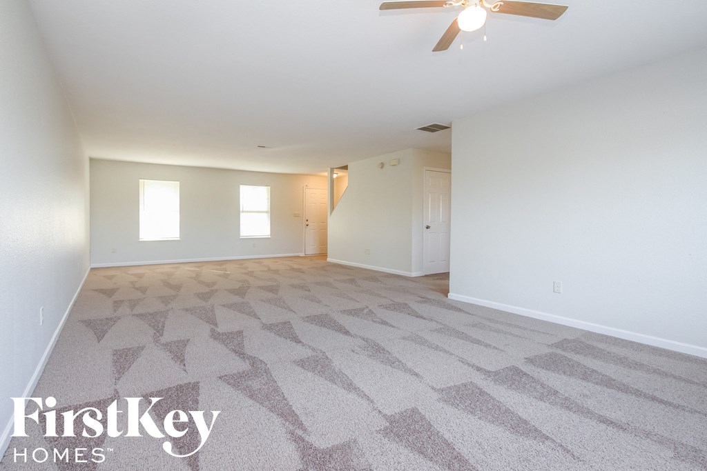 A spacious room with a carpeted floor and a ceiling fan.