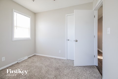 a bedroom with white walls and carpet and a door to a closet
