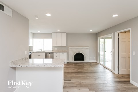A spacious living room with a fireplace and a kitchen in the background.