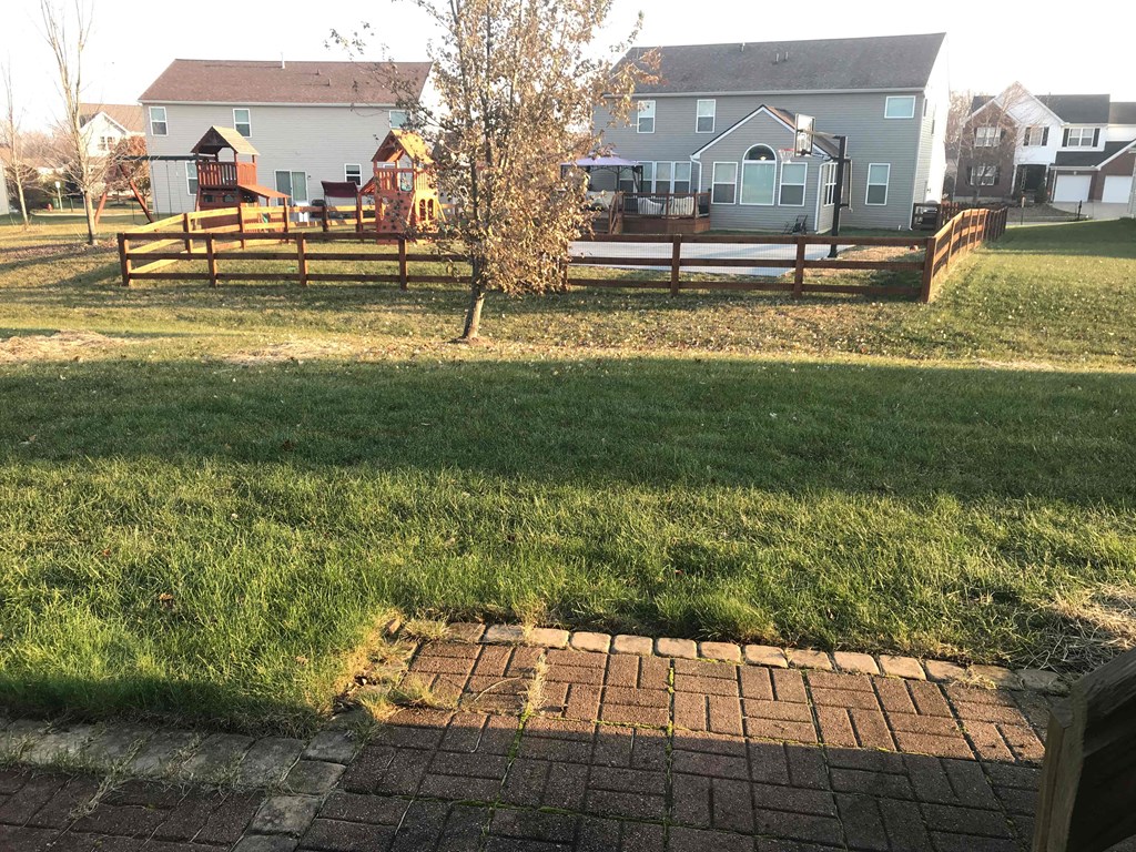 A backyard with a brick walkway and a wooden fence.