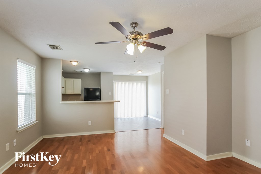 an empty living room with a ceiling fan and a kitchen