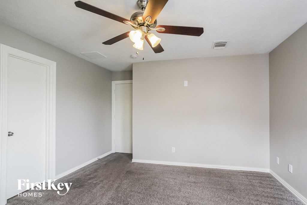 an empty living room with a ceiling fan and a white wall