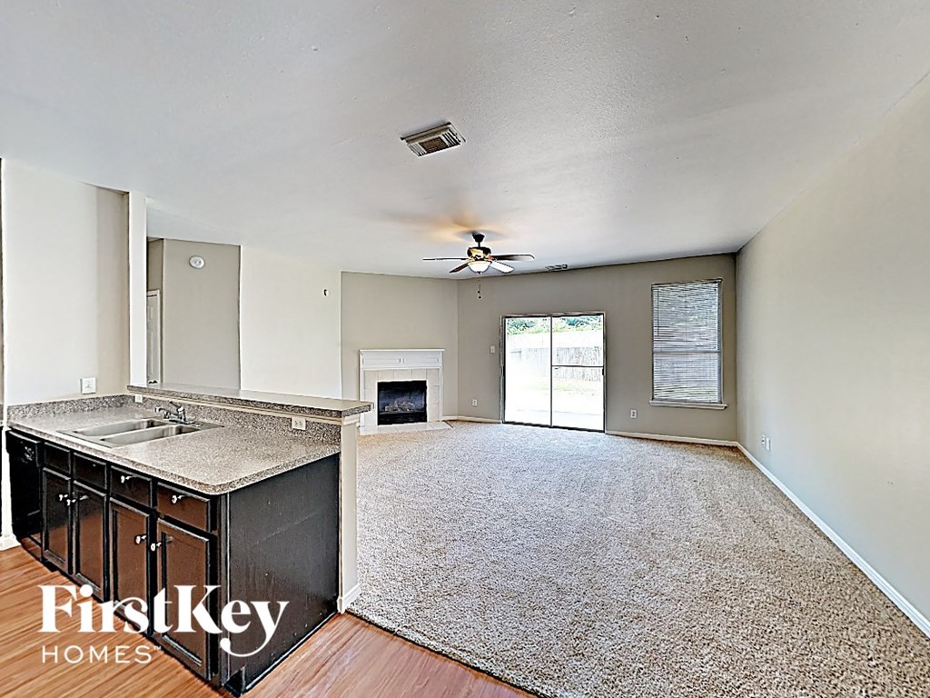 an empty living room with a kitchen and a ceiling fan
