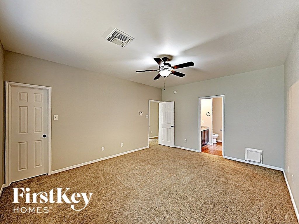 an empty living room with a ceiling fan and a door to a bathroom