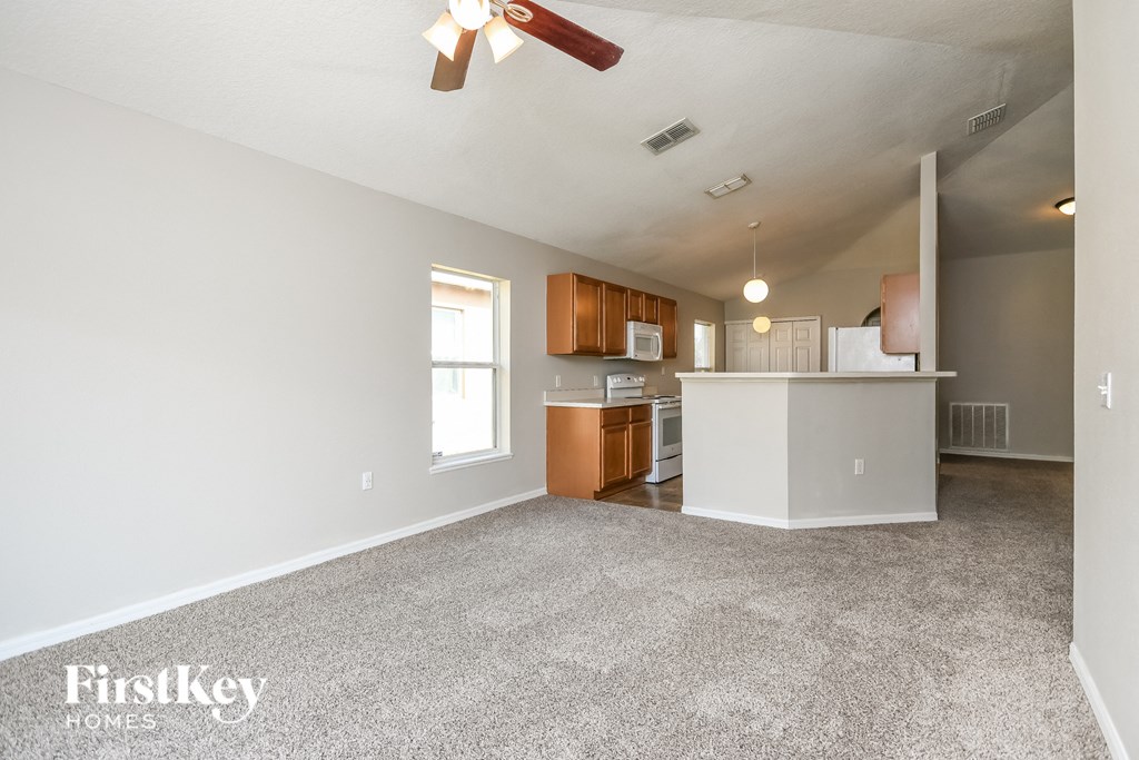 an empty living room with a kitchen and a ceiling fan