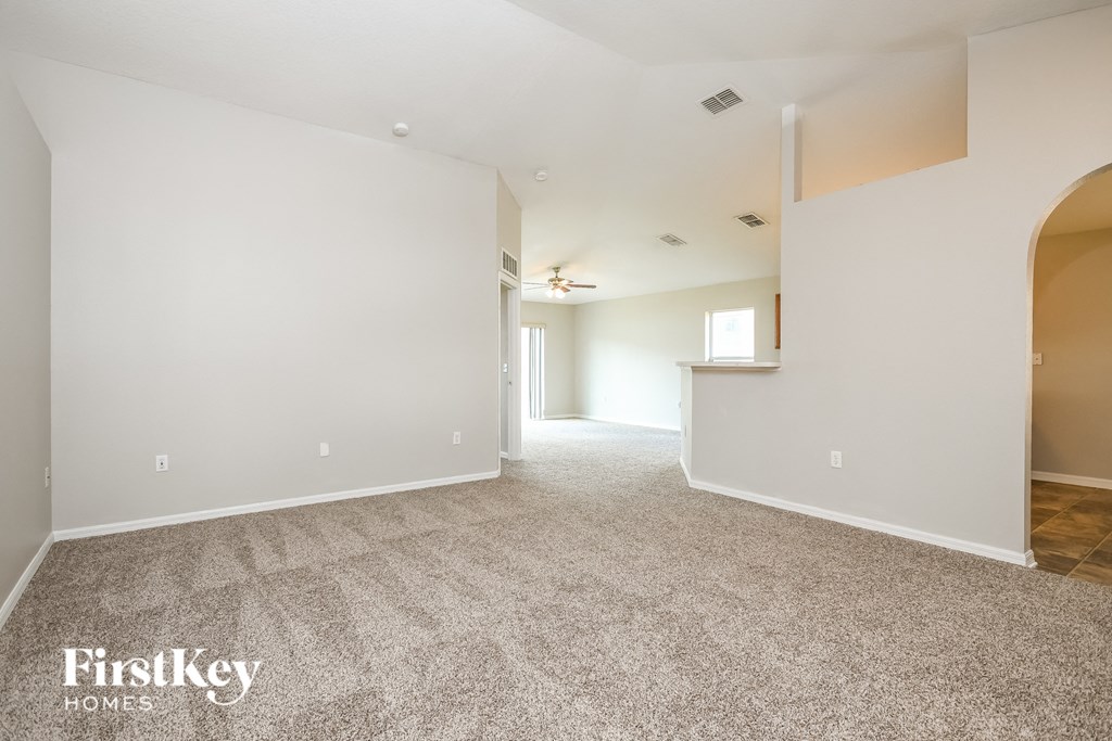 the spacious living room and dining room with white walls and carpet