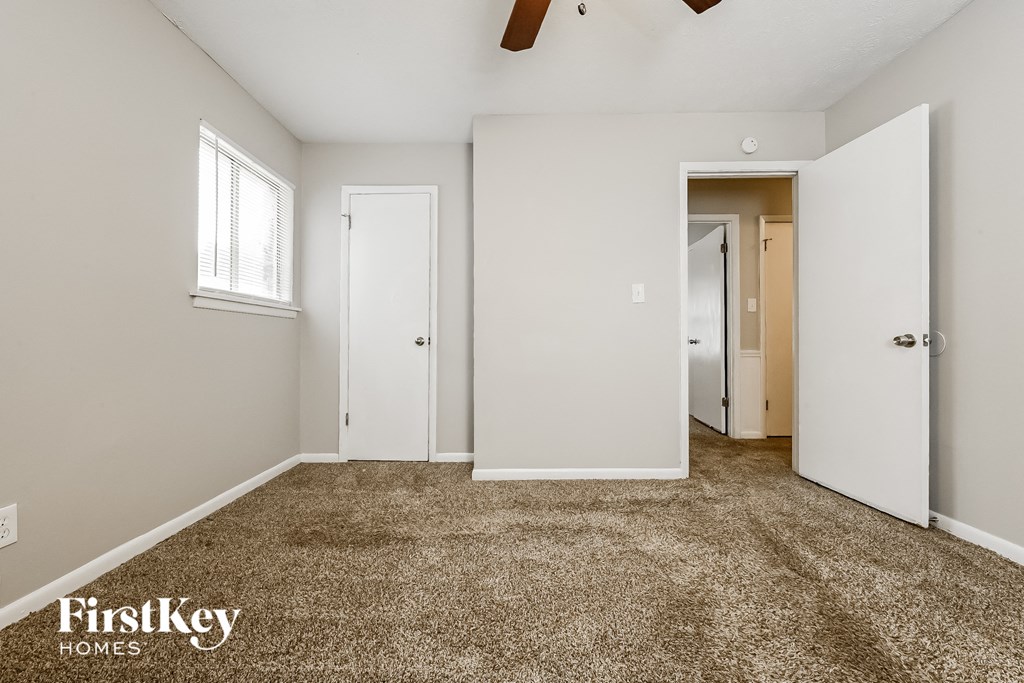 a bedroom with white walls and carpet and a door to a closet