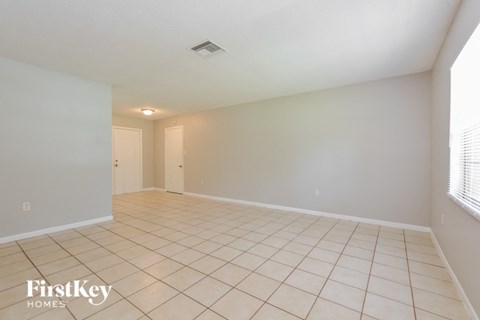 an empty living room with tiled flooring and a door to a hallway