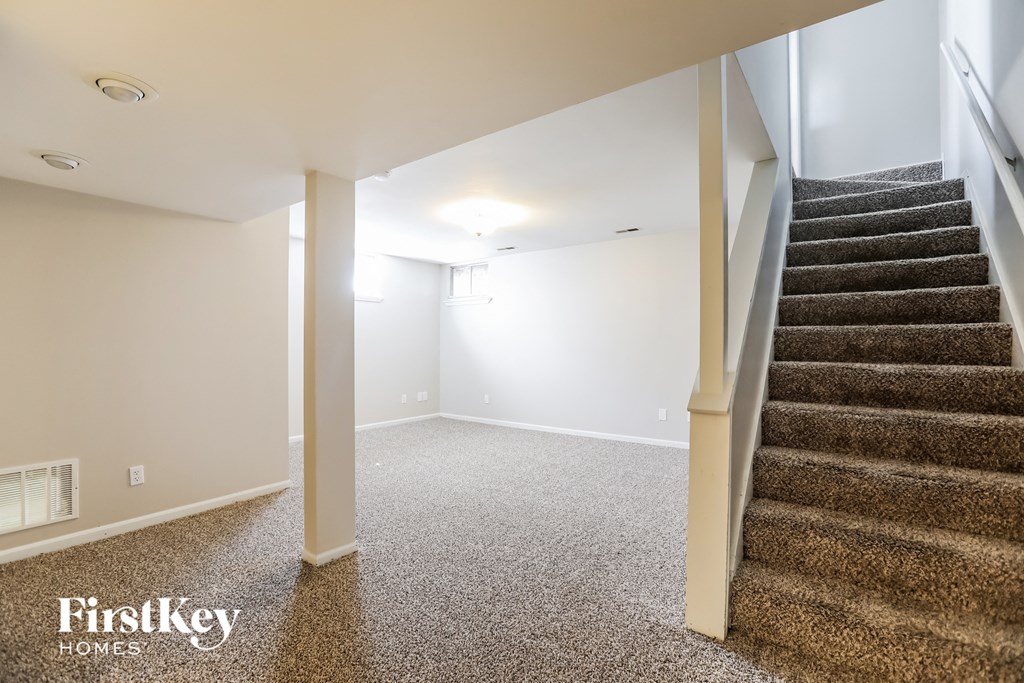 a basement with a staircase and carpeted stairs    and a white wall