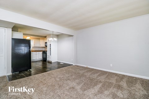 A spacious room with a carpeted floor and a black refrigerator.