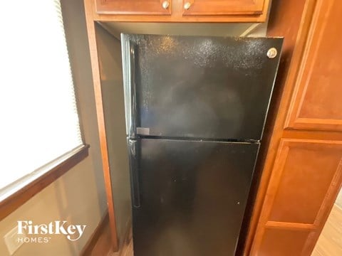 A black refrigerator is in a kitchen with wooden cabinets.