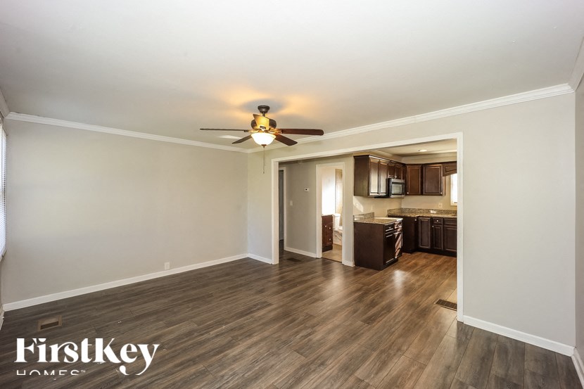 A spacious room with a ceiling fan and a kitchen area in the background.