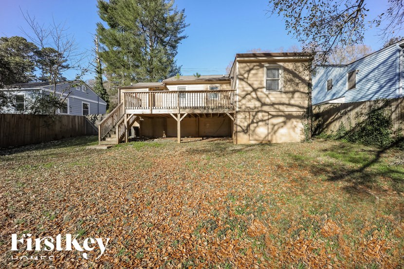 A house with a balcony is surrounded by trees and a fence.
