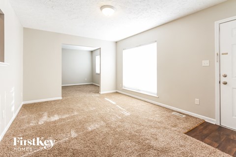 a spacious living room with carpet and a door to a bedroom