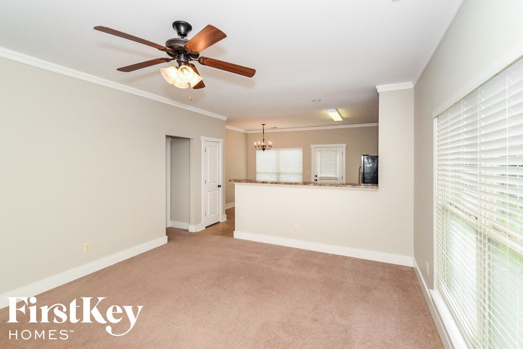 an empty living room with a ceiling fan and a kitchen