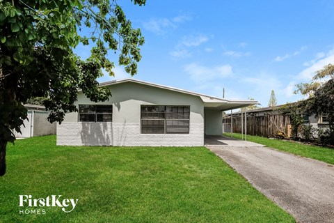 A house with a white exterior and a grey roof is surrounded by a green lawn.