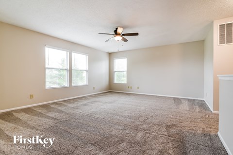 A spacious room with a carpeted floor and a ceiling fan.