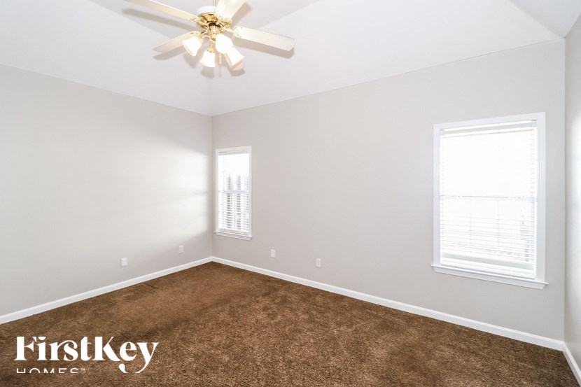 A room with a ceiling fan and two windows.